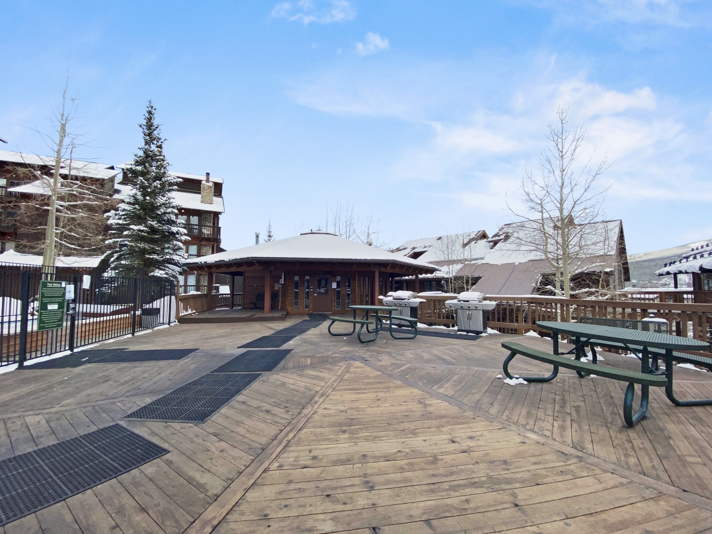 Expansive outdoor deck with picnic tables and BBQ facilities surrounded by snow-covered mountain resort buildings.