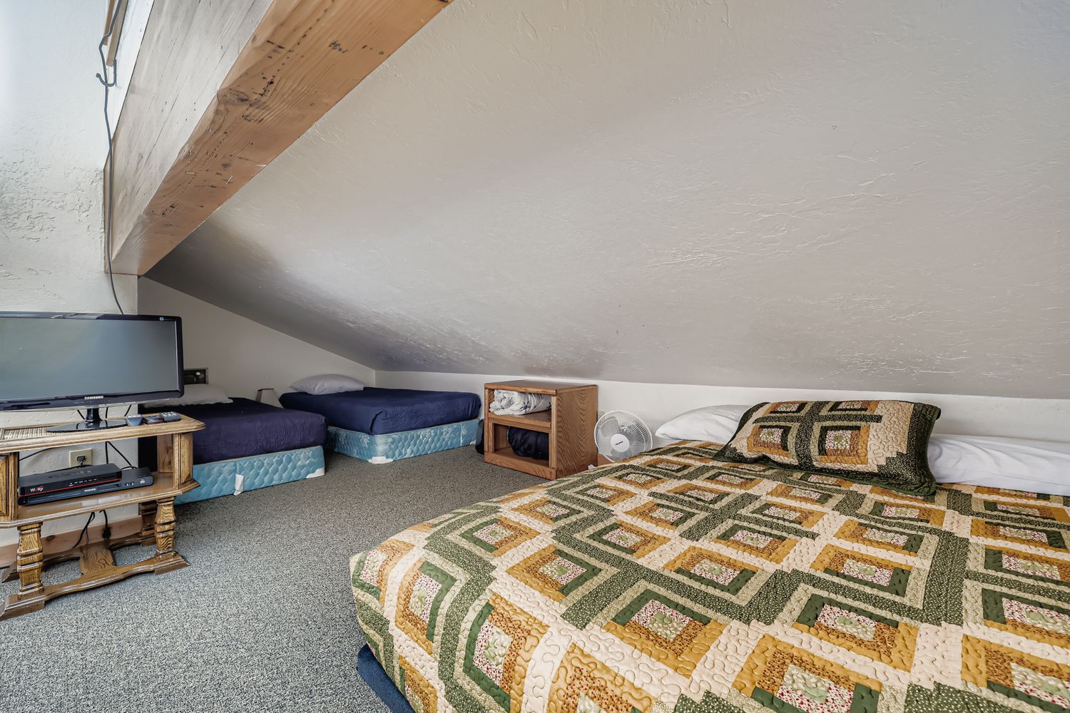 Cozy attic bedroom with rustic beams creates your perfect retreat, featuring comfortable beds and entertainment setup for relaxing evenings.