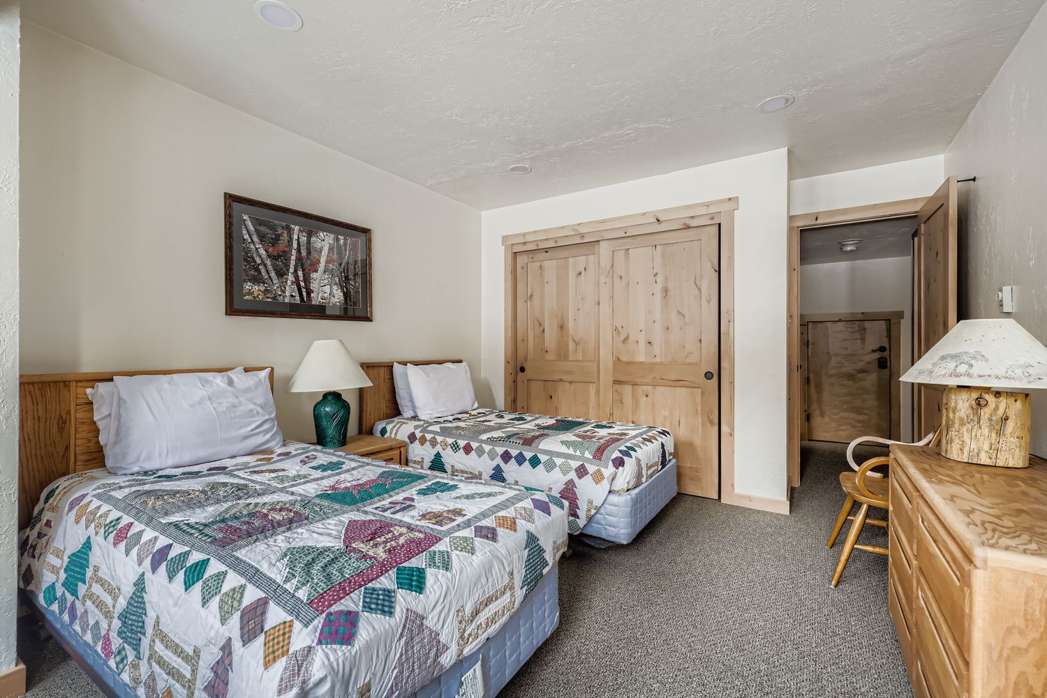 Cozy twin beds with handmade quilts await your mountain getaway, complete with rustic wood furnishings and peaceful forest artwork.