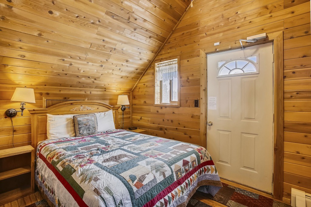 Your cozy cabin bedroom features warm wood walls, soft bedside lamps, and a handcrafted quilt for peaceful mountain nights.