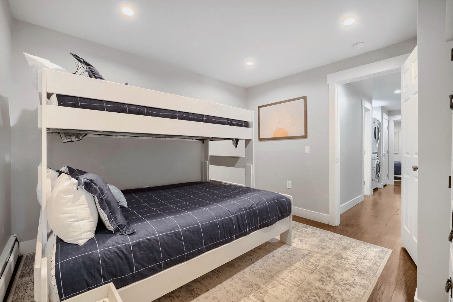 A cozy bedroom featuring a white bunk bed with stylish navy grid bedding, perfect for families or groups traveling together. Bright and modern with soft gray walls and warm wood floors.
