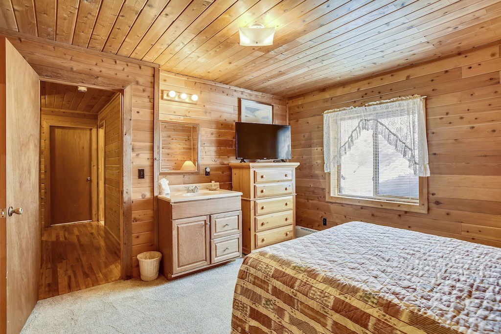 Unwind in your cozy cabin bedroom with rustic wood walls, a comfortable bed, and convenient vanity with mirror for getting ready.