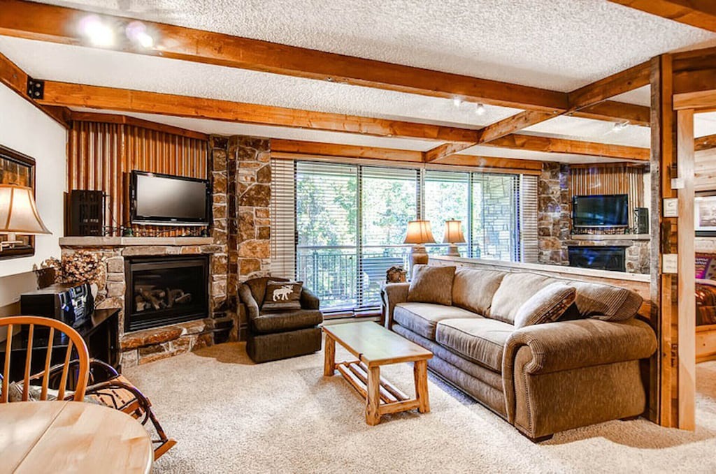 Unwind in your cozy living room with exposed beams, stone fireplace, and plush seating where comfort meets rustic elegance.