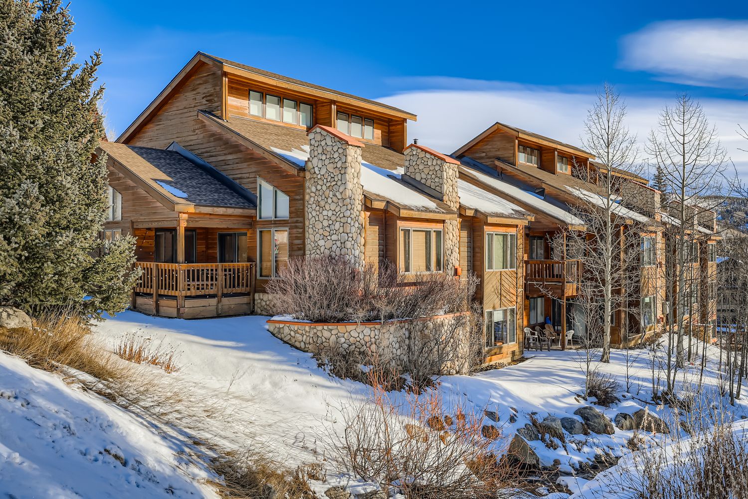 Mountain lodge featuring natural stone and wood architecture nestled in a snowy winter landscape with clear blue skies.
