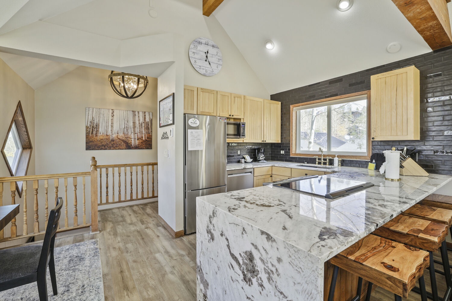 Your fully equipped kitchen features stunning marble countertops, modern appliances, and warm wood accents under soaring vaulted ceilings—perfect for preparing meals while enjoying natural light streaming through the windows.