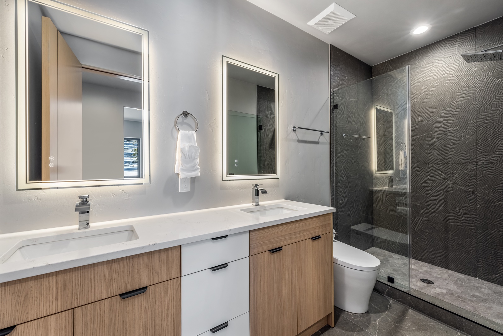 Unwind in your sophisticated bathroom with dual vanities, elegant mirrors, and a luxurious walk-in shower featuring stunning textured walls.