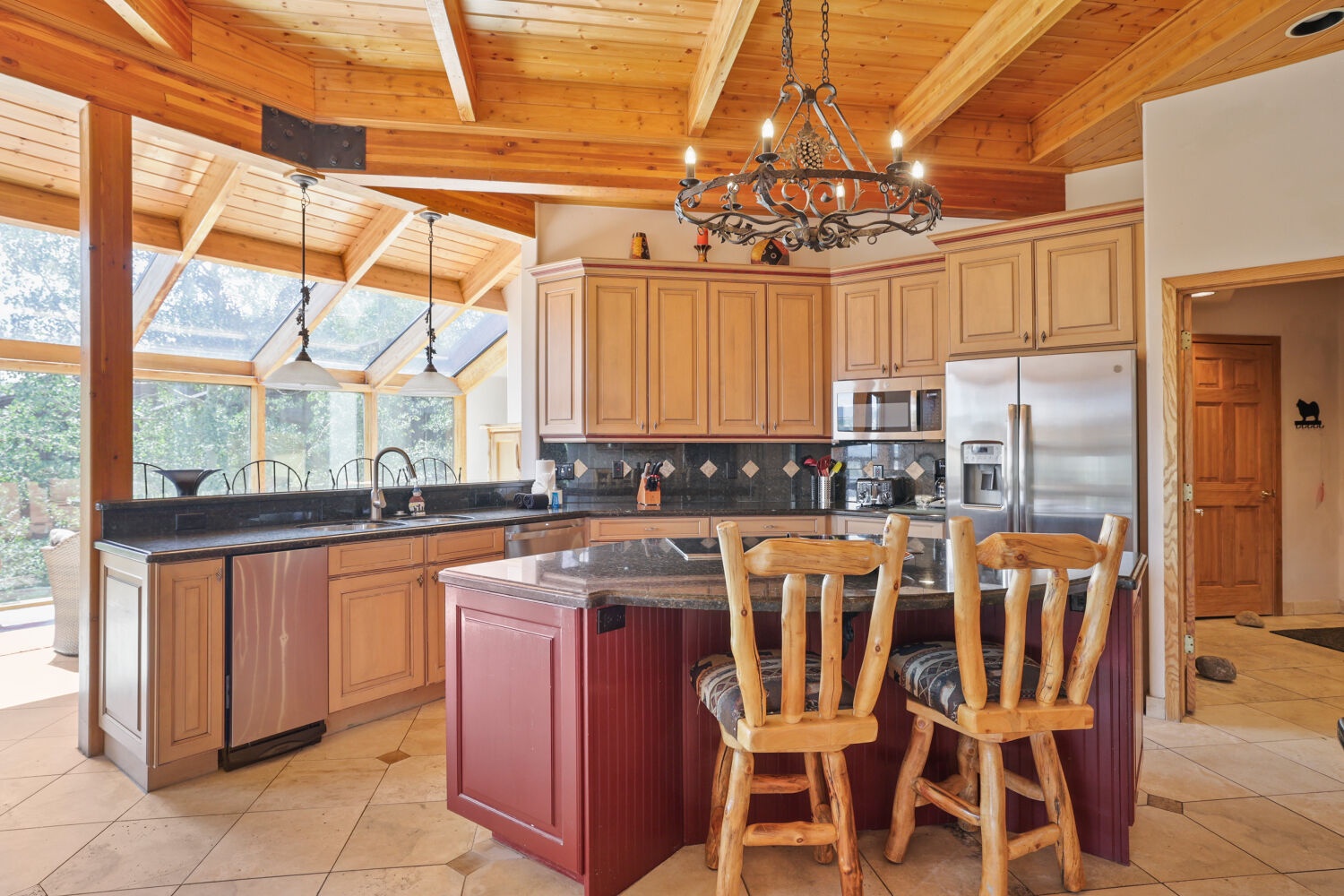 Spacious kitchen with soaring exposed wood beams and floor-to-ceiling windows. Granite island and rustic breakfast bar with warm wood tones create mountain-lodge charm.