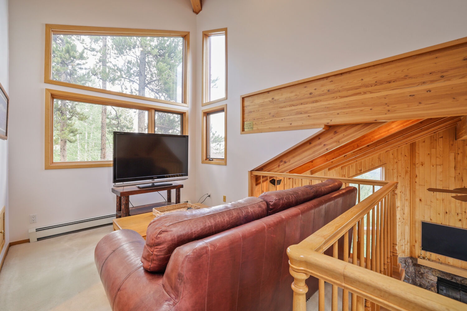 Relax on a cozy leather sofa while soaking in stunning treetop views through floor-to-ceiling windows. Your warm mountain retreat awaits with vaulted ceilings and natural wood charm.