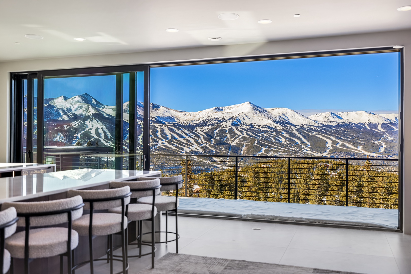 Savor your morning coffee while gazing at breathtaking mountain peaks through floor-to-ceiling windows in this stunning modern kitchen.