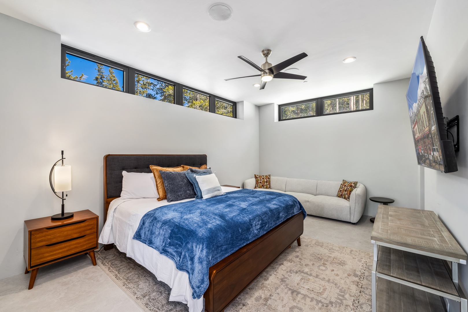 Unwind in your modern bedroom with plush bedding, cozy seating area, and natural light streaming through clerestory windows.