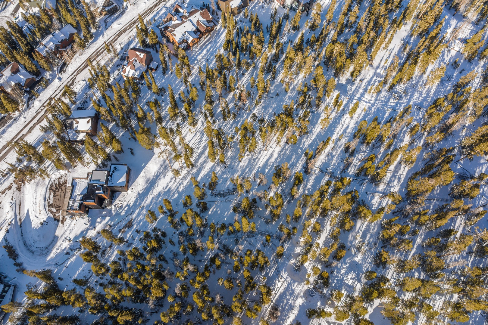 Aerial view of snow-covered mountain retreat nestled among evergreen trees in pristine winter landscape.