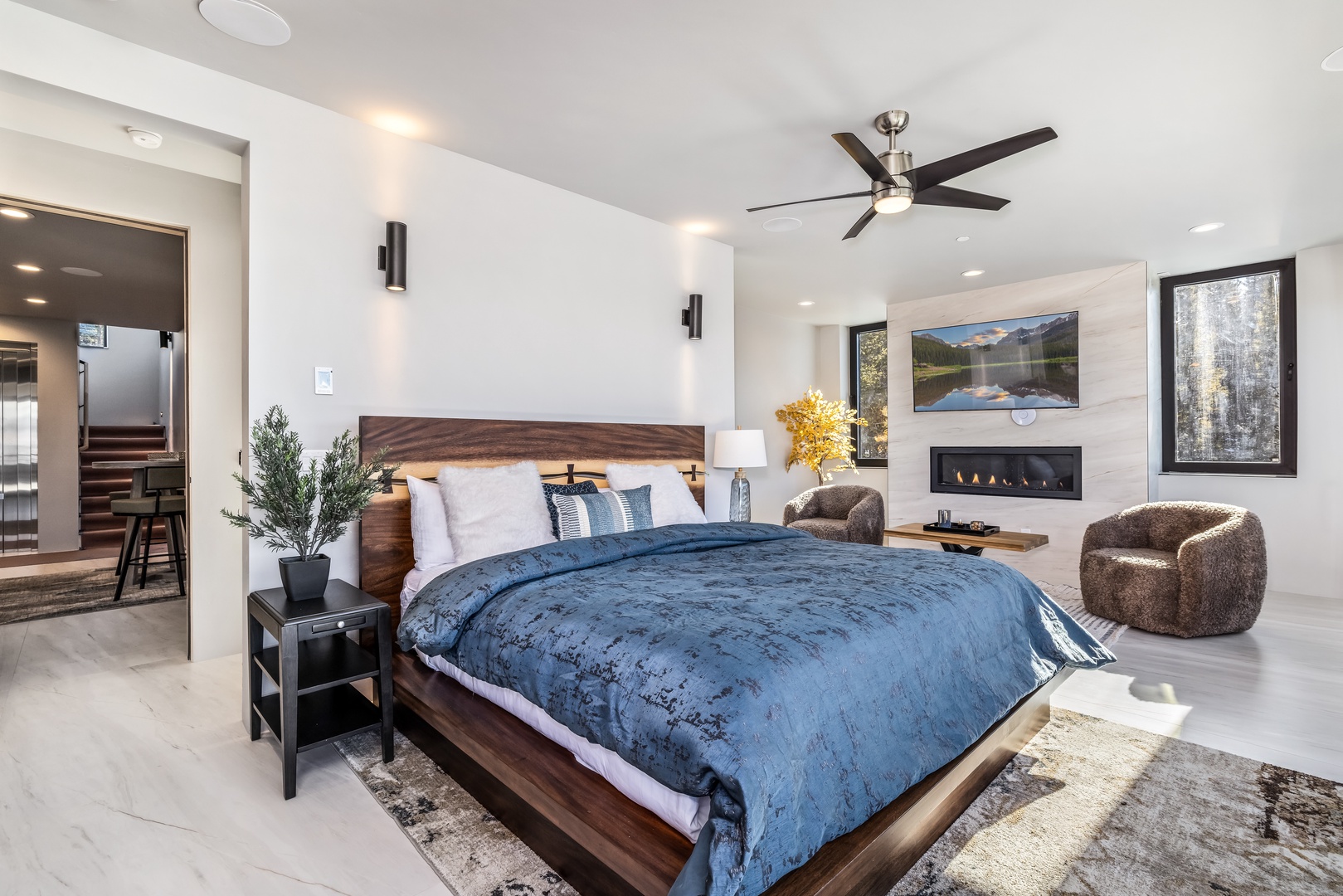 Unwind in your luxurious master suite featuring a cozy fireplace, modern ceiling fan, and elegant furniture for the perfect retreat.