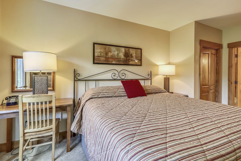 Unwind in your cozy bedroom featuring warm wood accents, comfortable striped bedding, and a convenient workspace for ultimate relaxation.