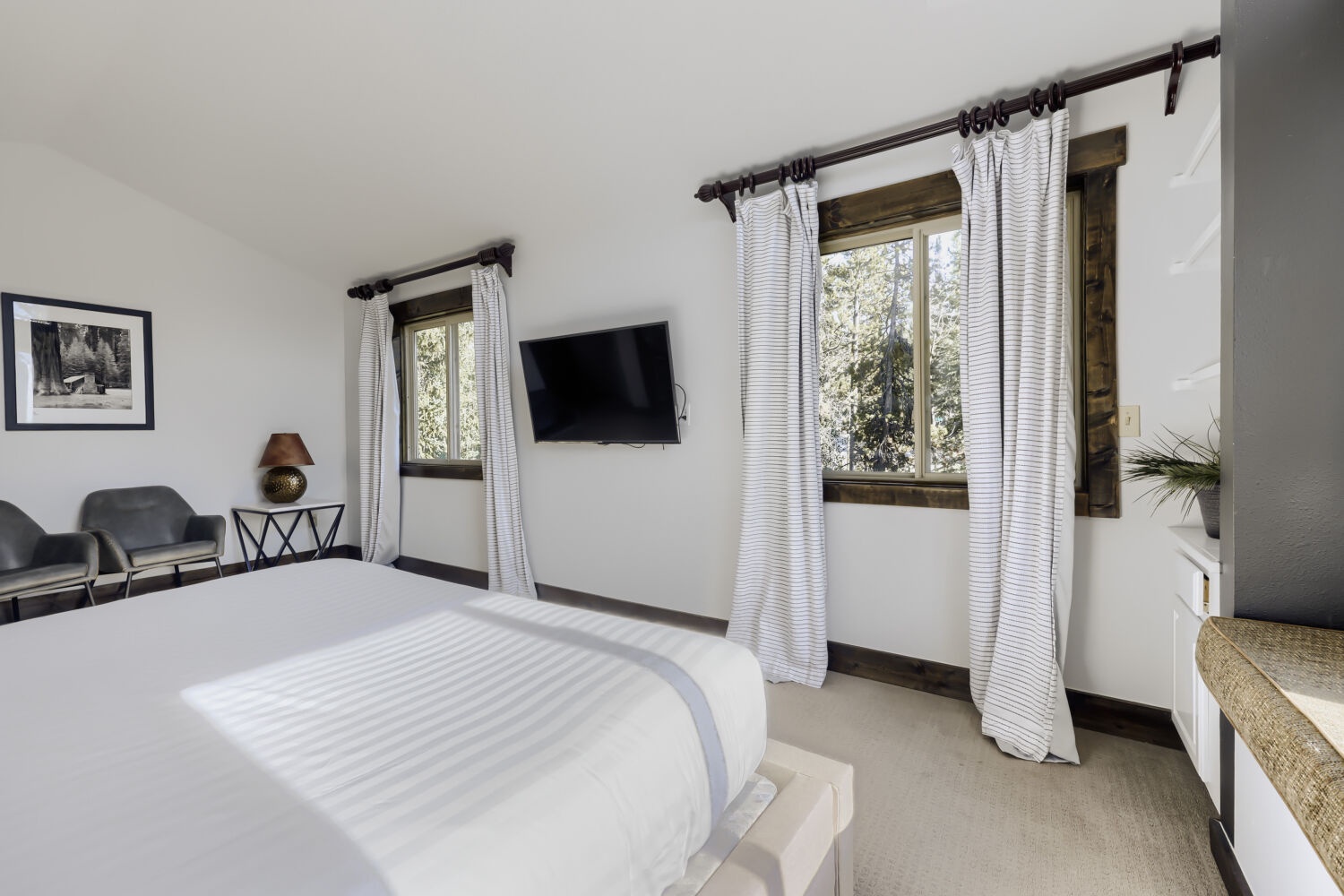 Relax in your peaceful bedroom with natural light streaming through windows framing views of green trees. Crisp linens, modern amenities, and a cozy sitting area invite you to unwind.