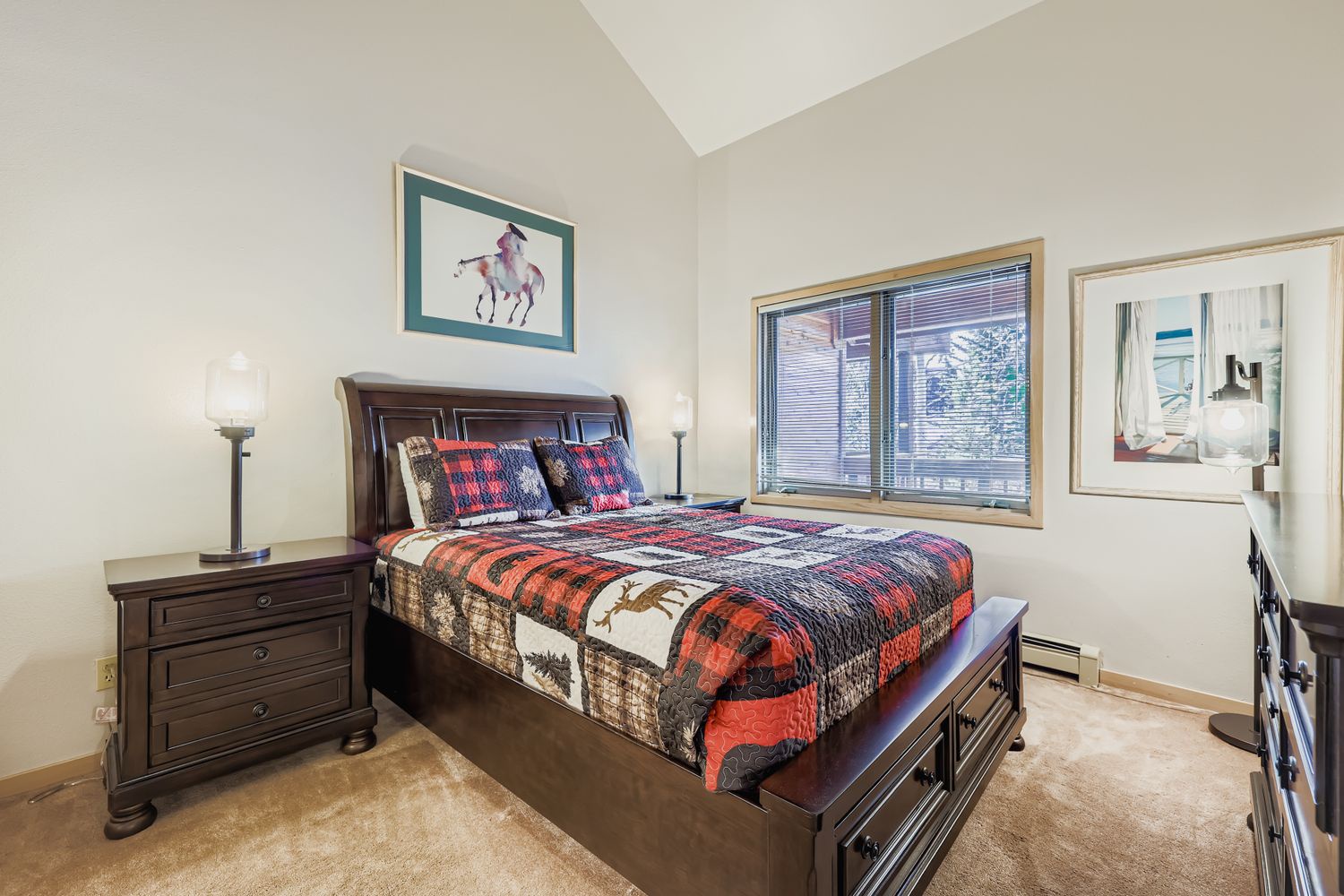 Drift off in this cozy bedroom featuring a plush quilted bed, rich wooden furniture, and peaceful mountain views through your window.