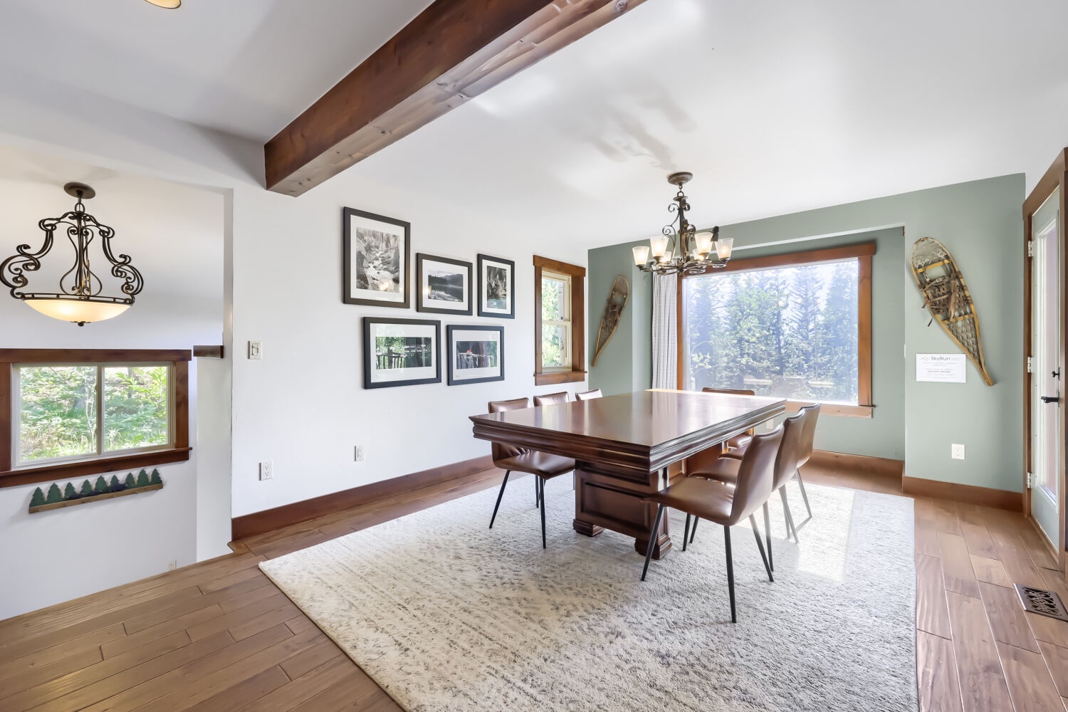 Gather around the handsome dining table under rustic beams, where you'll savor meals with stunning forest views framed by the window—a cozy, inviting space that feels like home.