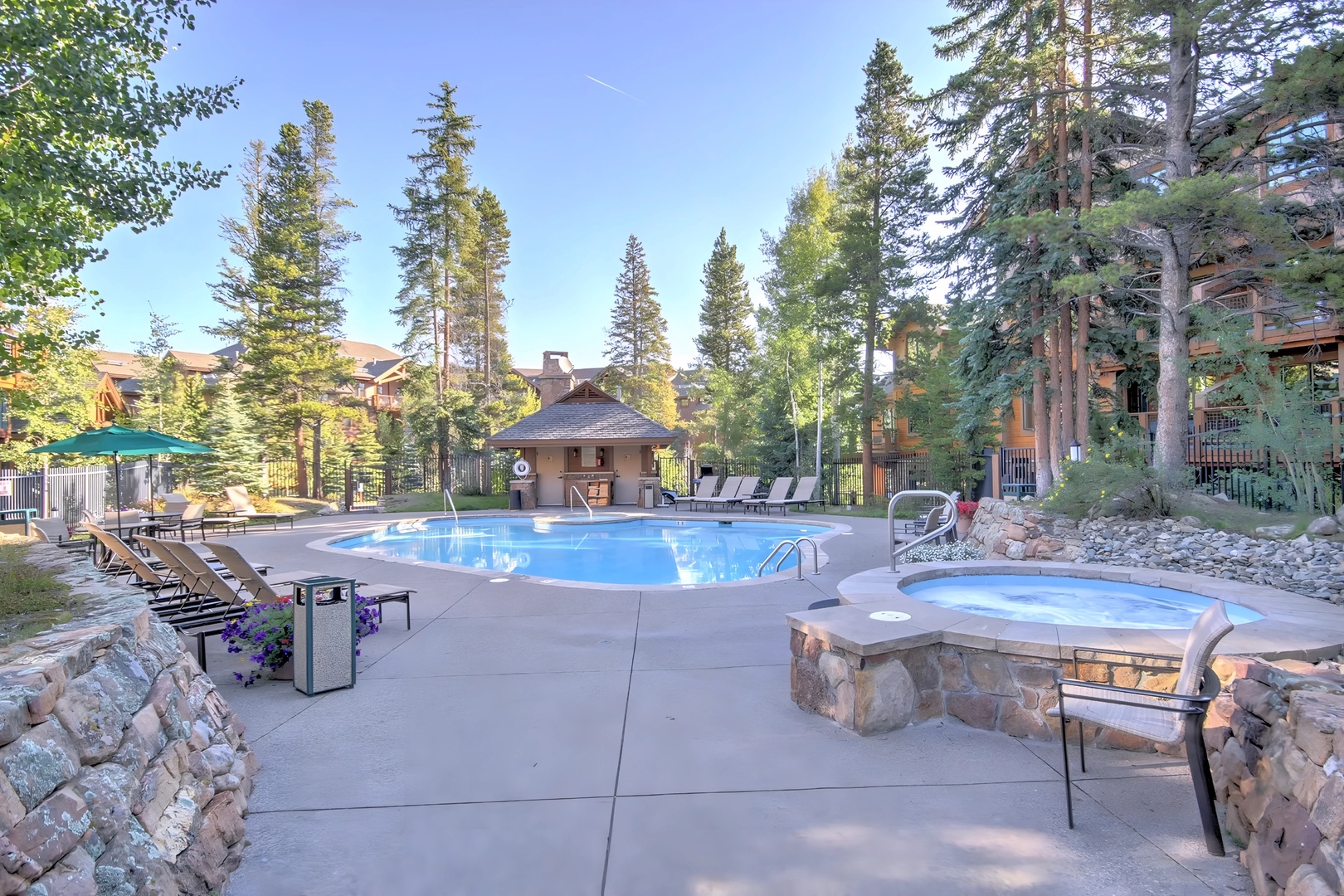 Mountain resort pool and spa area surrounded by tall pine trees and alpine architecture.