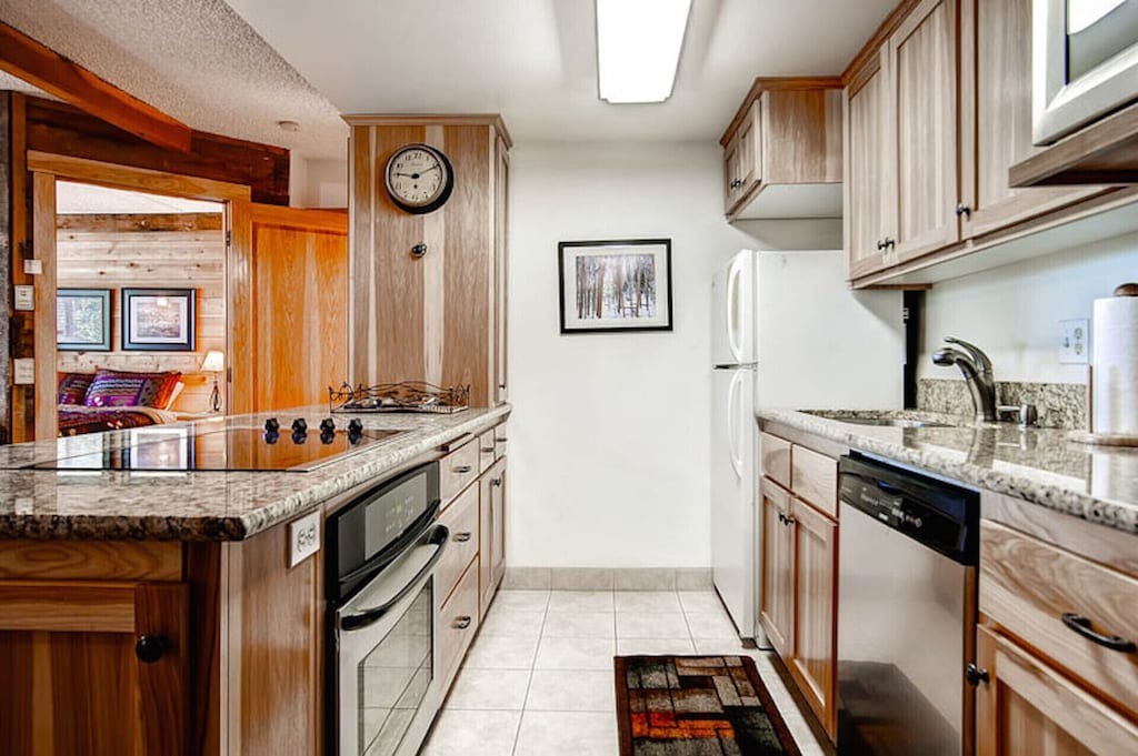 Prepare your favorite meals in this fully-equipped galley kitchen featuring granite countertops, modern appliances, and warm wood cabinetry.