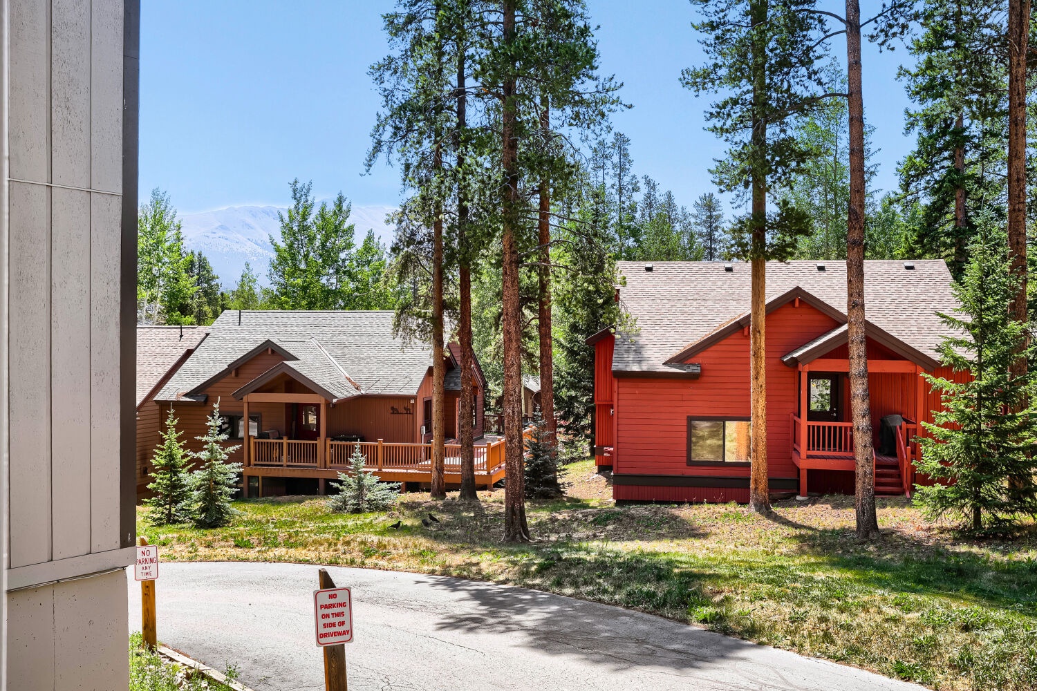 A forested mountain vacation rental community with private cabins nestled among tall pines, featuring traditional architecture and natural landscaping near mountain peaks.