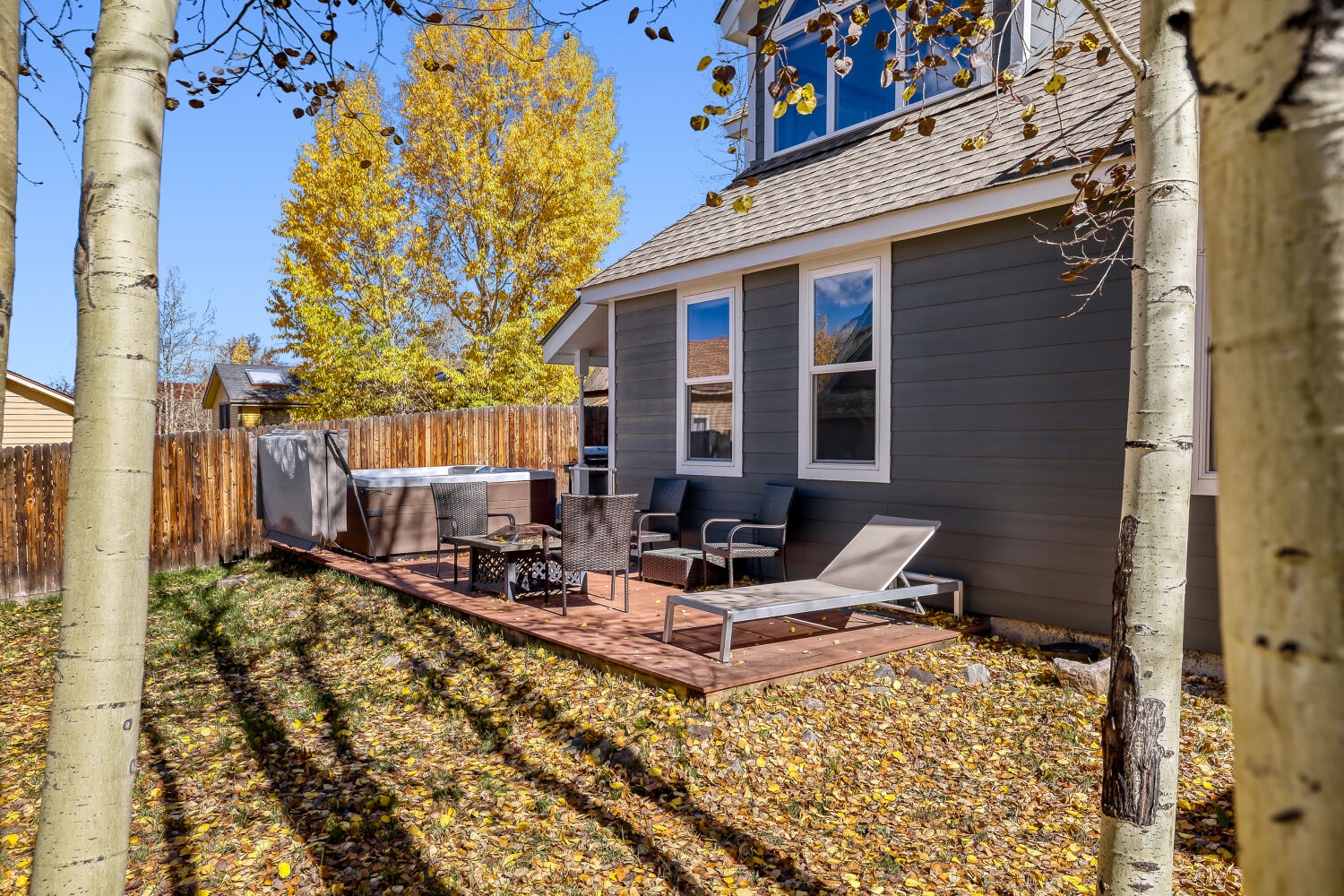 Modern rental home framed by golden aspens and backed by mountain views, featuring a cozy deck with seating and sunbeds in a quiet autumn setting.