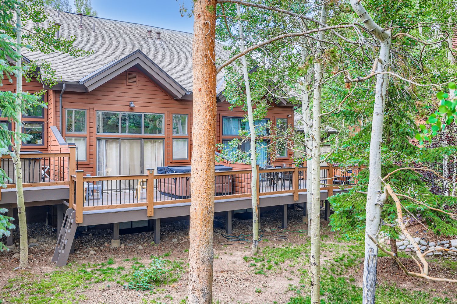 A charming mountain retreat nestled among towering trees, featuring warm wood siding and an inviting wraparound deck.