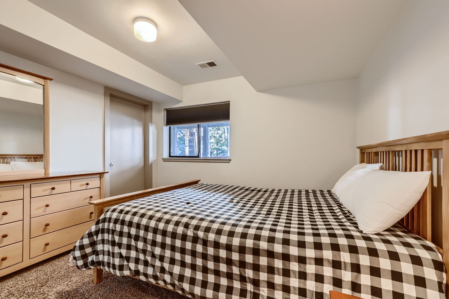 Cozy bedroom with warm wood furnishings, plaid bedding, and forest views through your window for peaceful mountain retreat vibes.