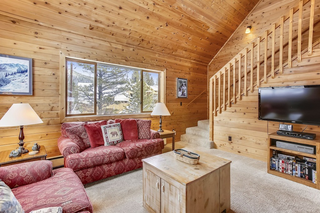 Cozy up in your rustic cabin living room with warm wood walls, comfortable red sofas, and mountain views.