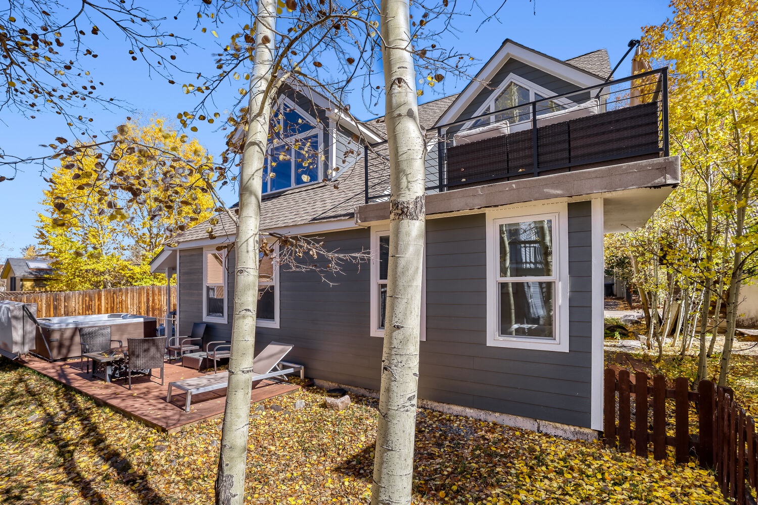 Modern mountain home featuring a private deck with hot tub, surrounded by golden aspens and backed by mature trees—a peaceful autumn retreat in a quiet neighborhood.