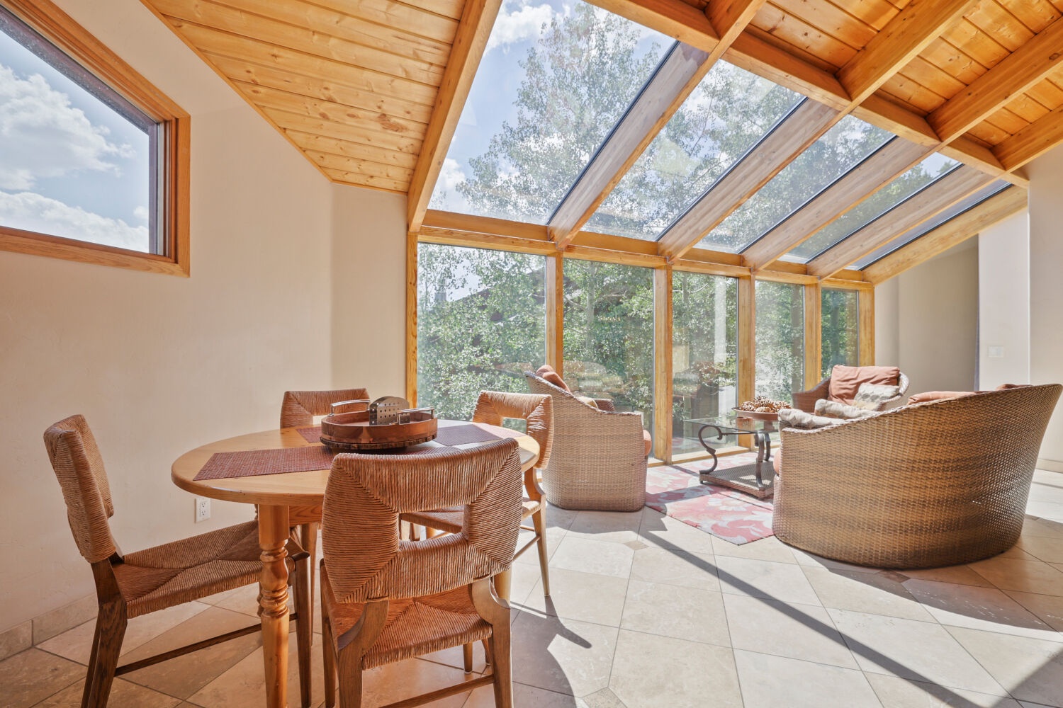Relax in your sun-drenched solarium where warm wood beams and floor-to-ceiling windows invite natural light to fill every corner. Enjoy peaceful garden views while lounging on comfortable wicker seating.