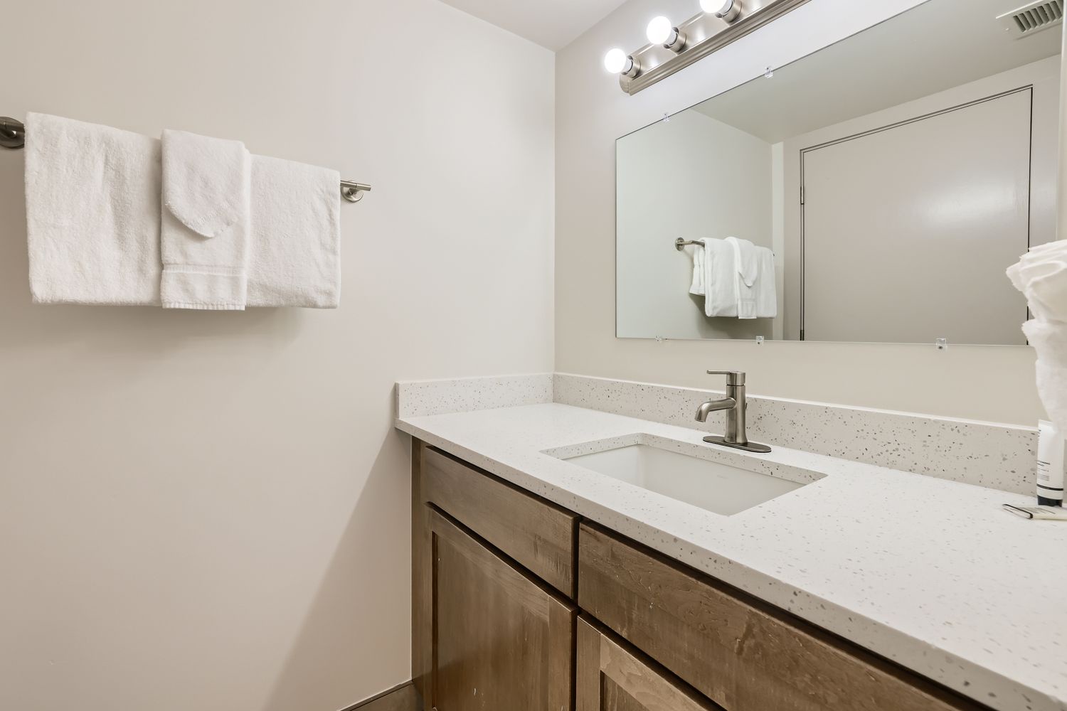 Step into your modern bathroom featuring elegant quartz countertops, warm wood vanity, and fresh towels awaiting your arrival.