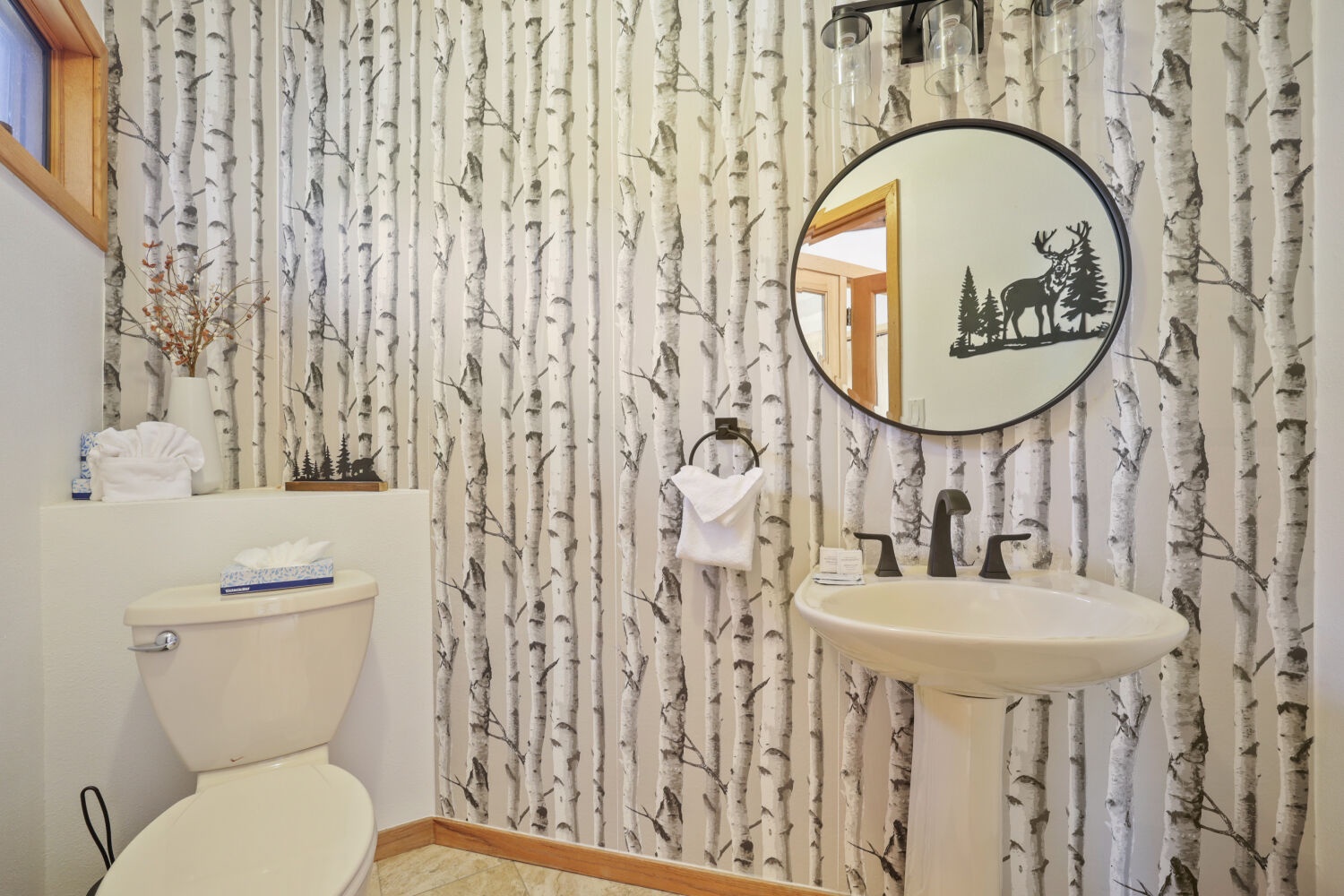 Step into your own woodland retreat with birch-patterned walls that bring the forest indoors. The rustic mirror and pedestal sink add charm to this cozy, nature-inspired bathroom.