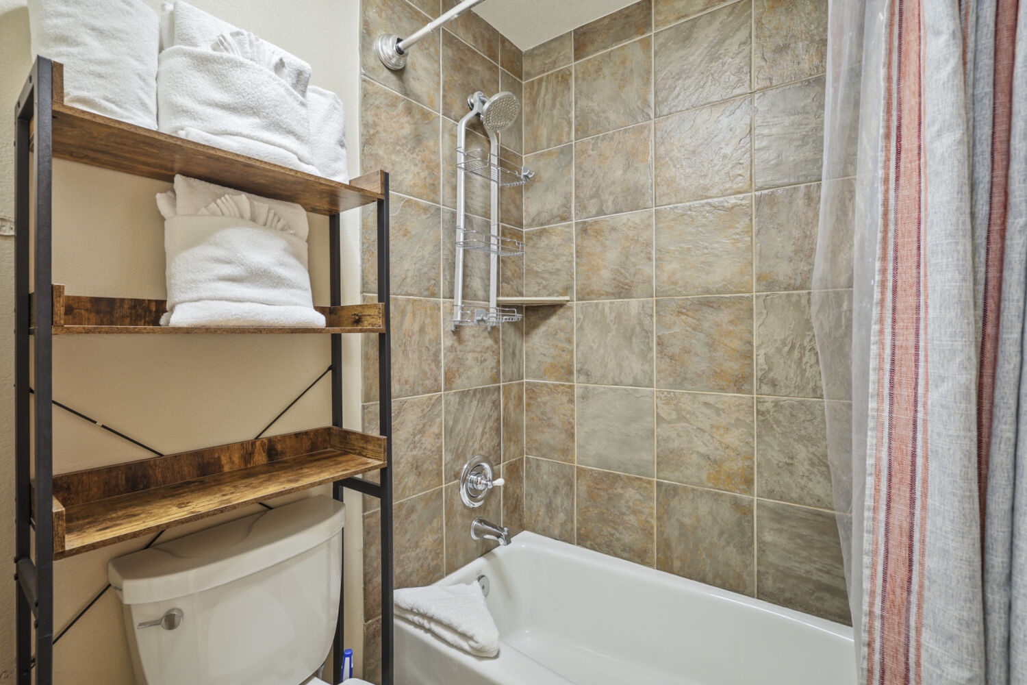 Step into your fresh, tiled bathroom with a combination tub and shower. Plush white towels await on rustic wood shelving, and everything you need is within reach.