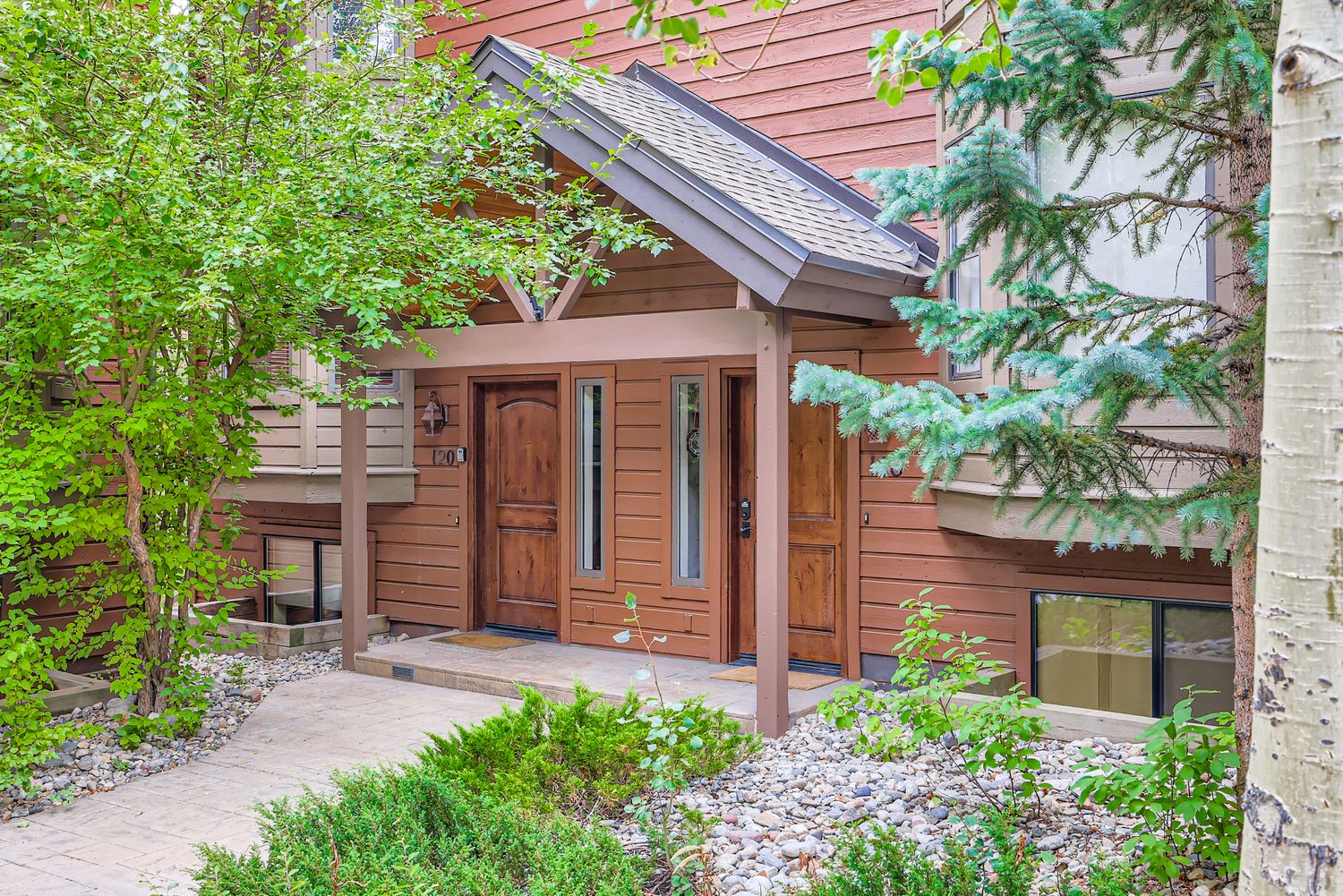Charming mountain retreat entrance surrounded by lush greenery and mature trees creates a welcoming first impression.