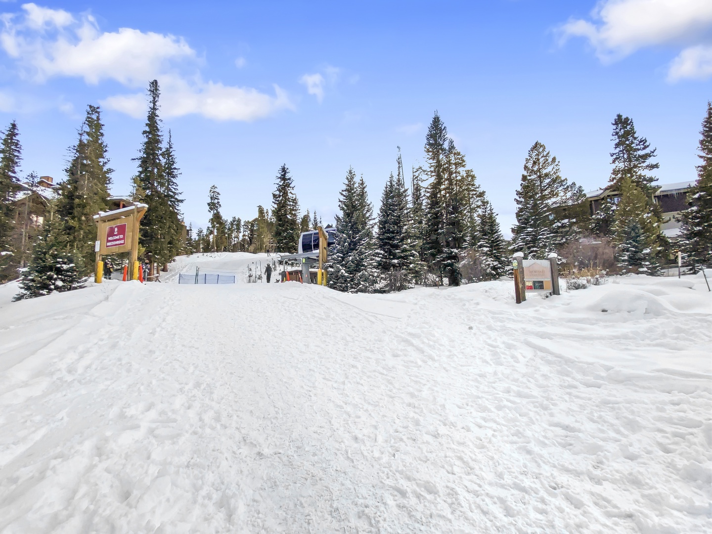 Snow-covered ski area surrounded by alpine evergreens and mountain lodges under bright winter skies.
