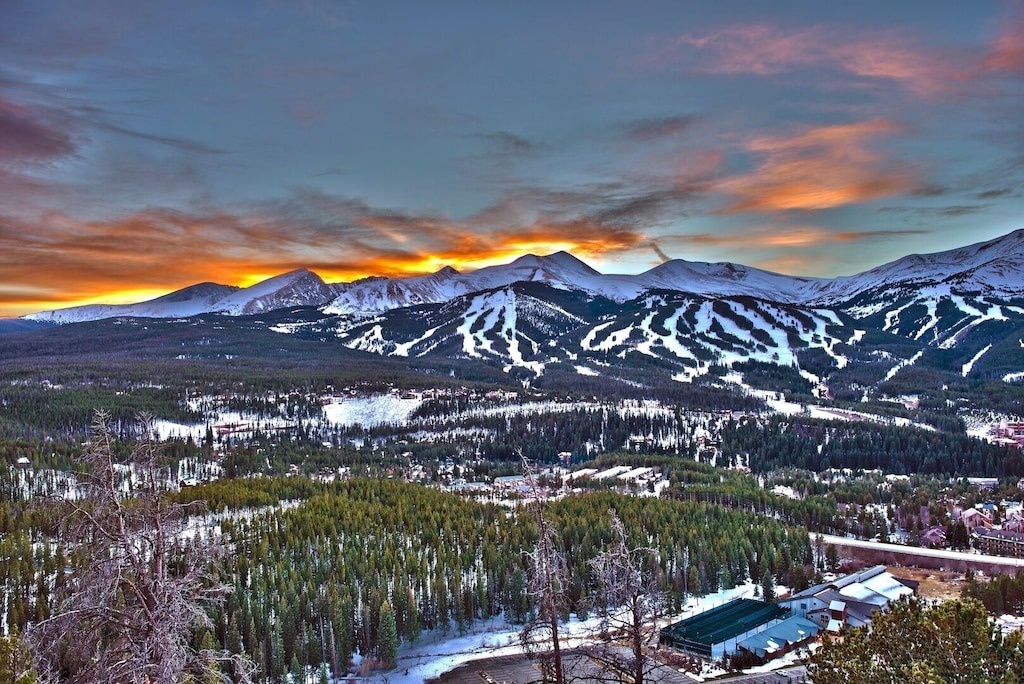 Spectacular mountain resort sunset illuminates snow-covered ski slopes and forested valley in this breathtaking alpine setting.