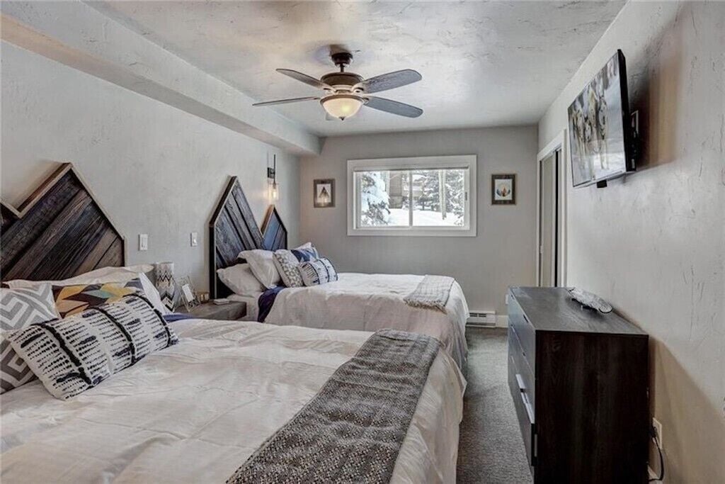 Drift off in this cozy twin bedroom with rustic mountain headboards, ceiling fan, and peaceful window views.