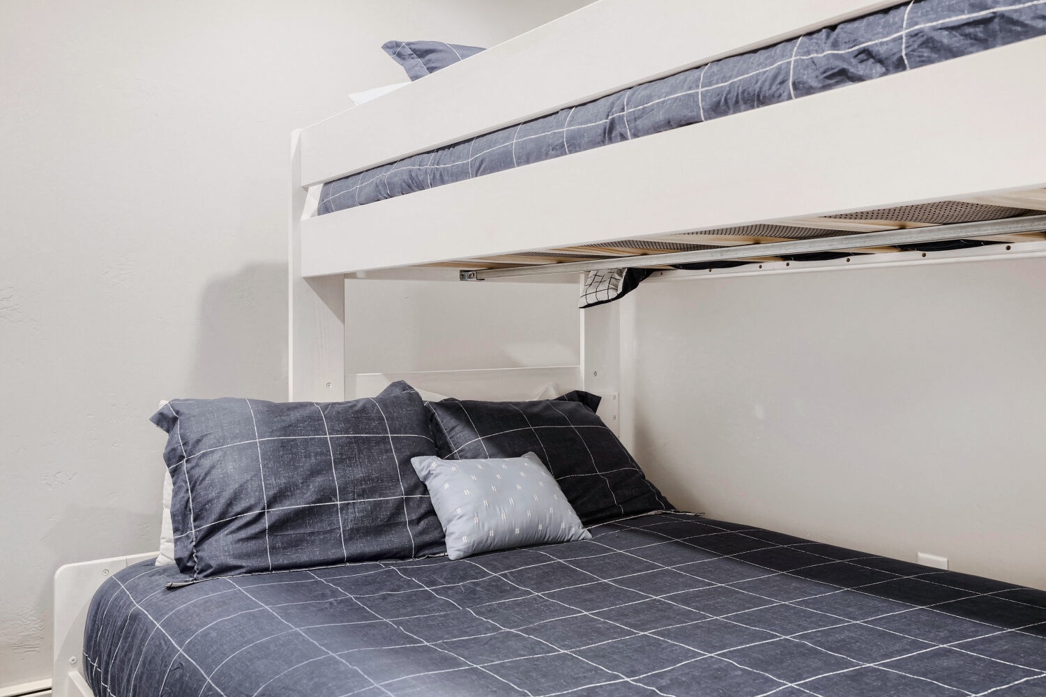 Crisp white bunk beds with stylish gray plaid linens create a cozy sleeping space perfect for your family's stay, offering comfort and modern simplicity.
