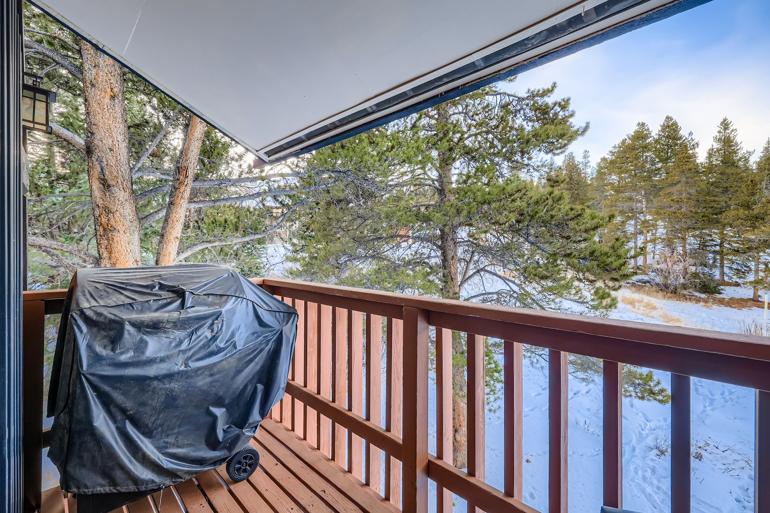 Covered balcony with winter forest views and outdoor grill for year-round relaxation.