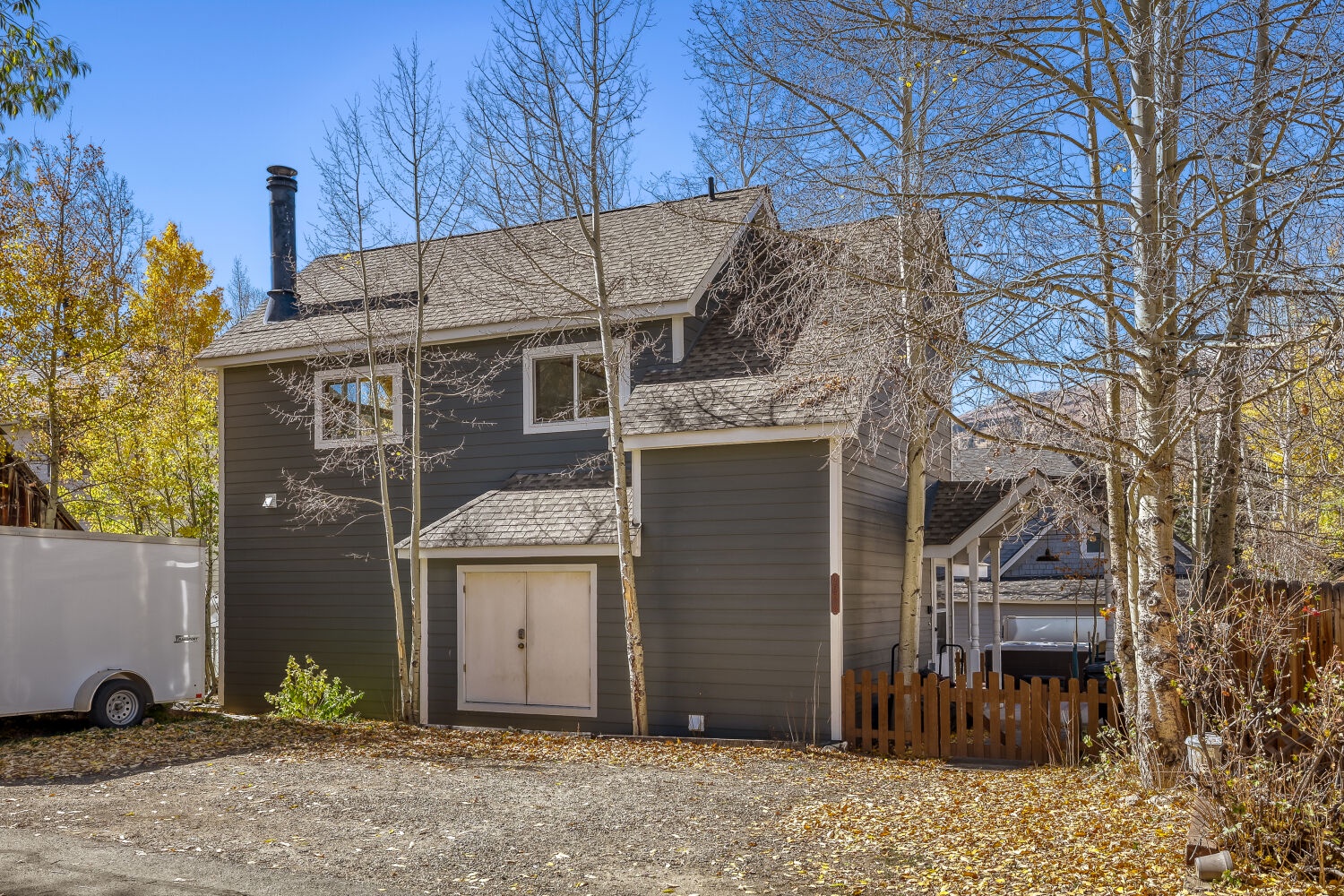 The property sits nestled among golden aspens and towering trees with seasonal fall foliage framing a charming mountain retreat against clear blue skies.