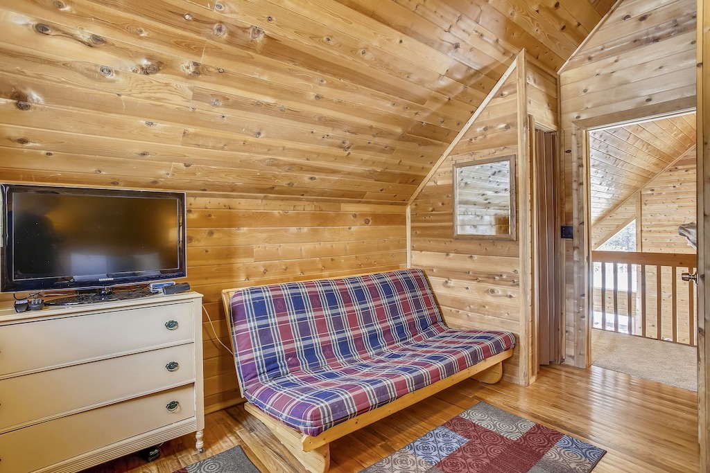Your cozy loft hideaway features warm wood walls, plaid seating, and a TV for relaxing mountain evenings together.