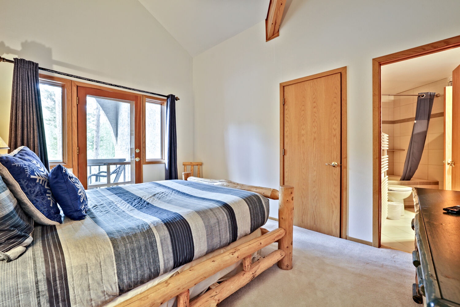 Your private bedroom features a cozy log-style bed with vaulted ceilings and direct balcony access with natural forest views through the door.