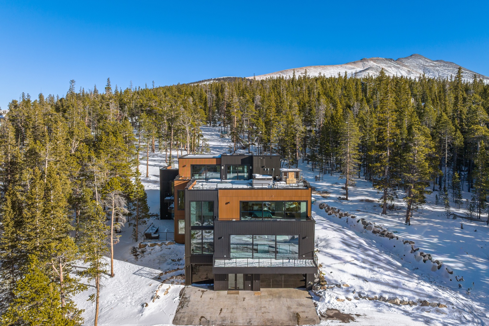 Modern mountain retreat nestled in pristine winter landscape with snow-capped peaks and forest views.