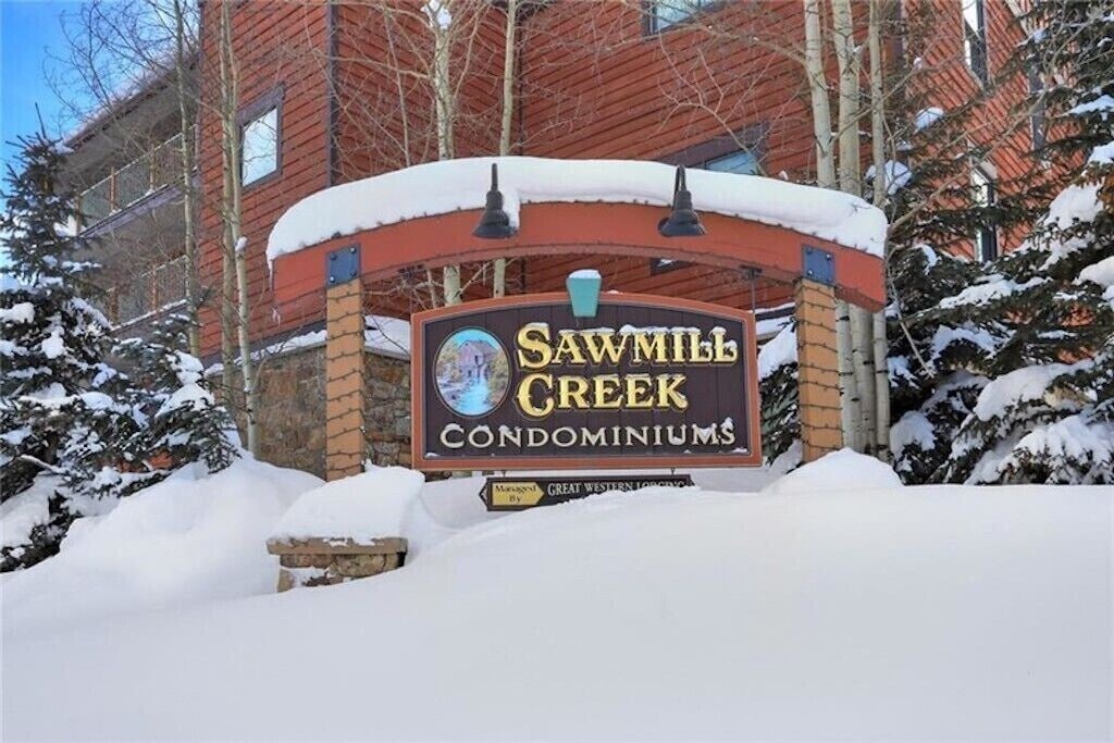 Snow-covered entrance sign welcomes visitors to Sawmill Creek Condominiums, nestled among towering pine trees in a pristine winter setting.