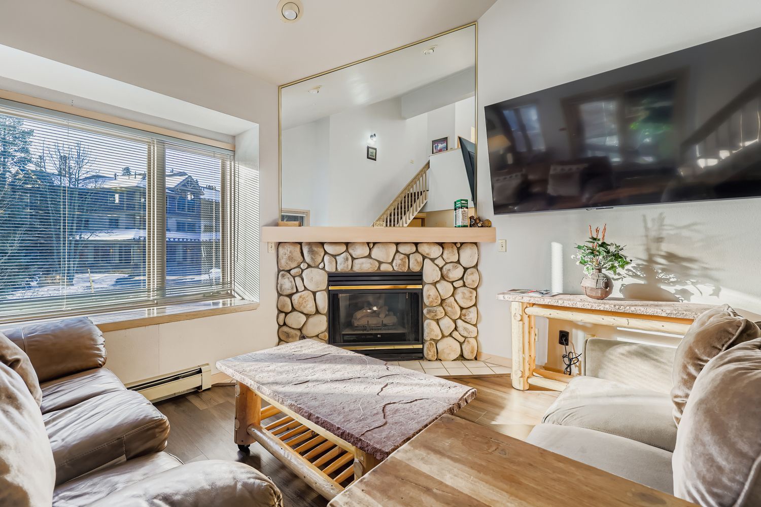 Unwind in your cozy living space with a stunning stone fireplace, comfortable seating, and warm natural light flowing through large windows.