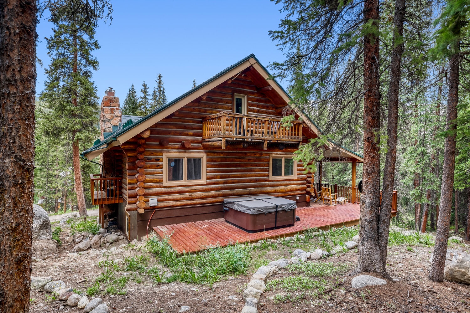 A rustic log cabin nestled among towering pines, offering a secluded mountain retreat with a private hot tub on the deck.