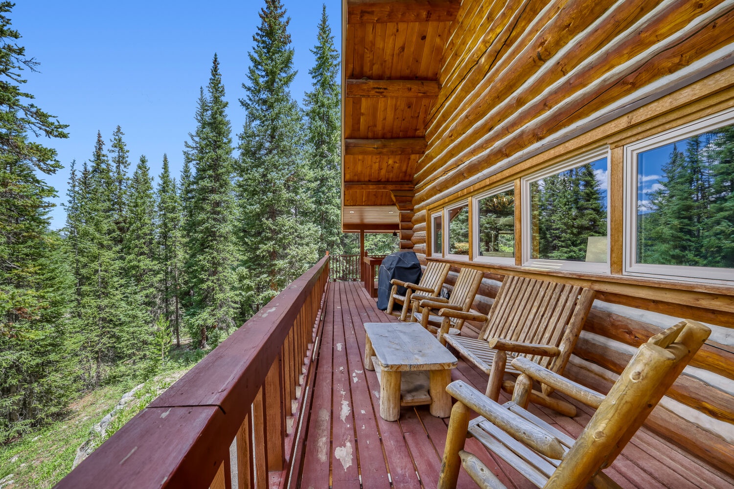 Wrap-around deck with handcrafted log furniture overlooking a forested hillside, perfect for morning coffee or unwinding after a day of adventure.