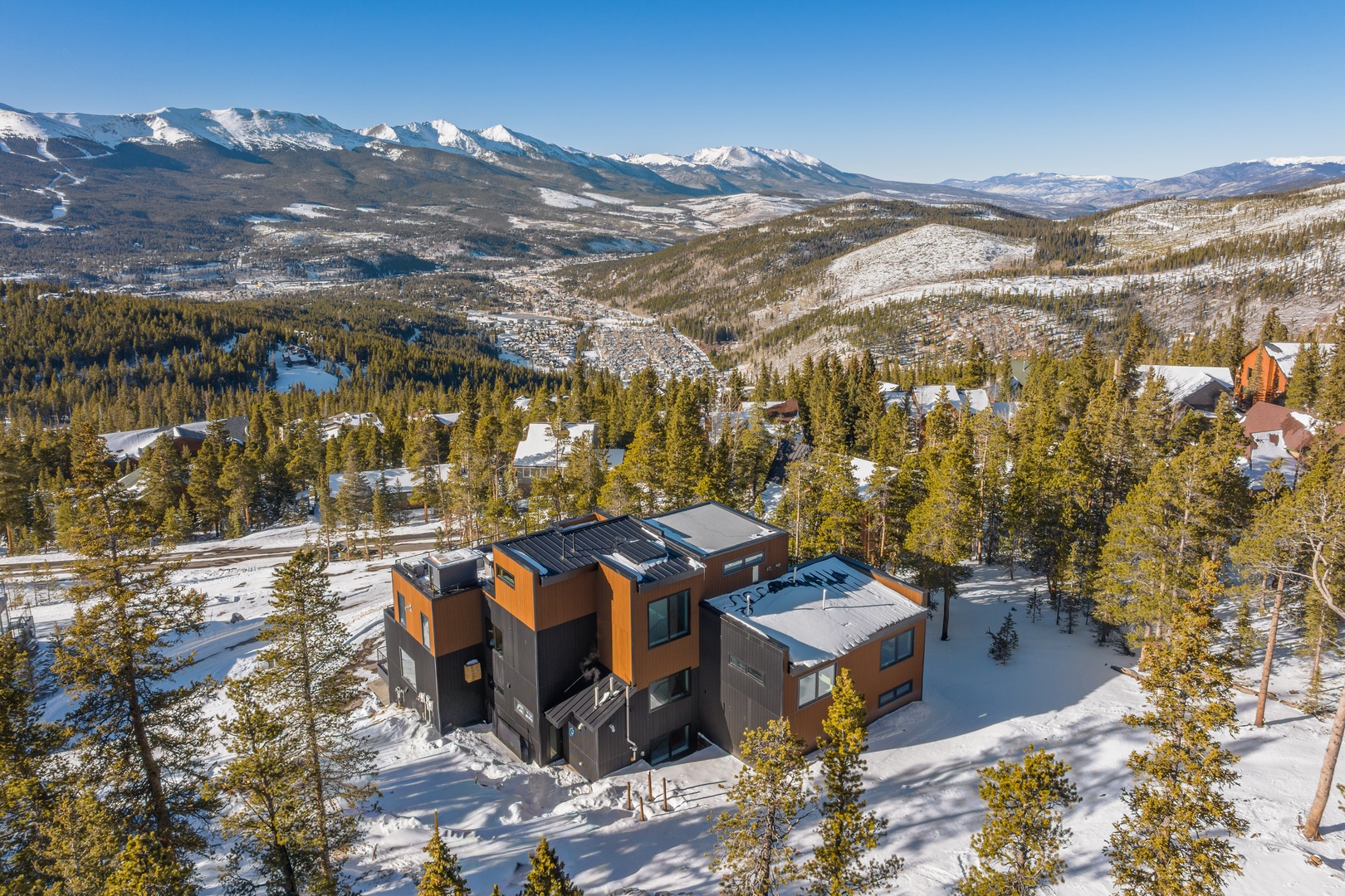 Modern mountain retreat nestled in pristine winter wonderland with dramatic snow-capped peaks and expansive valley views stretching to the horizon.
