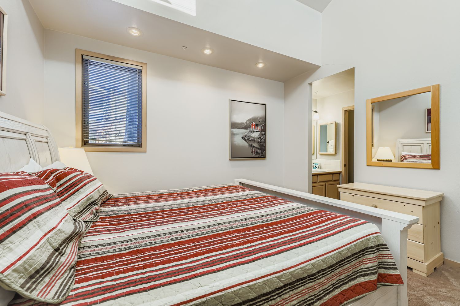 Unwind in your bright bedroom featuring a comfortable bed with colorful striped linens and modern furnishings.