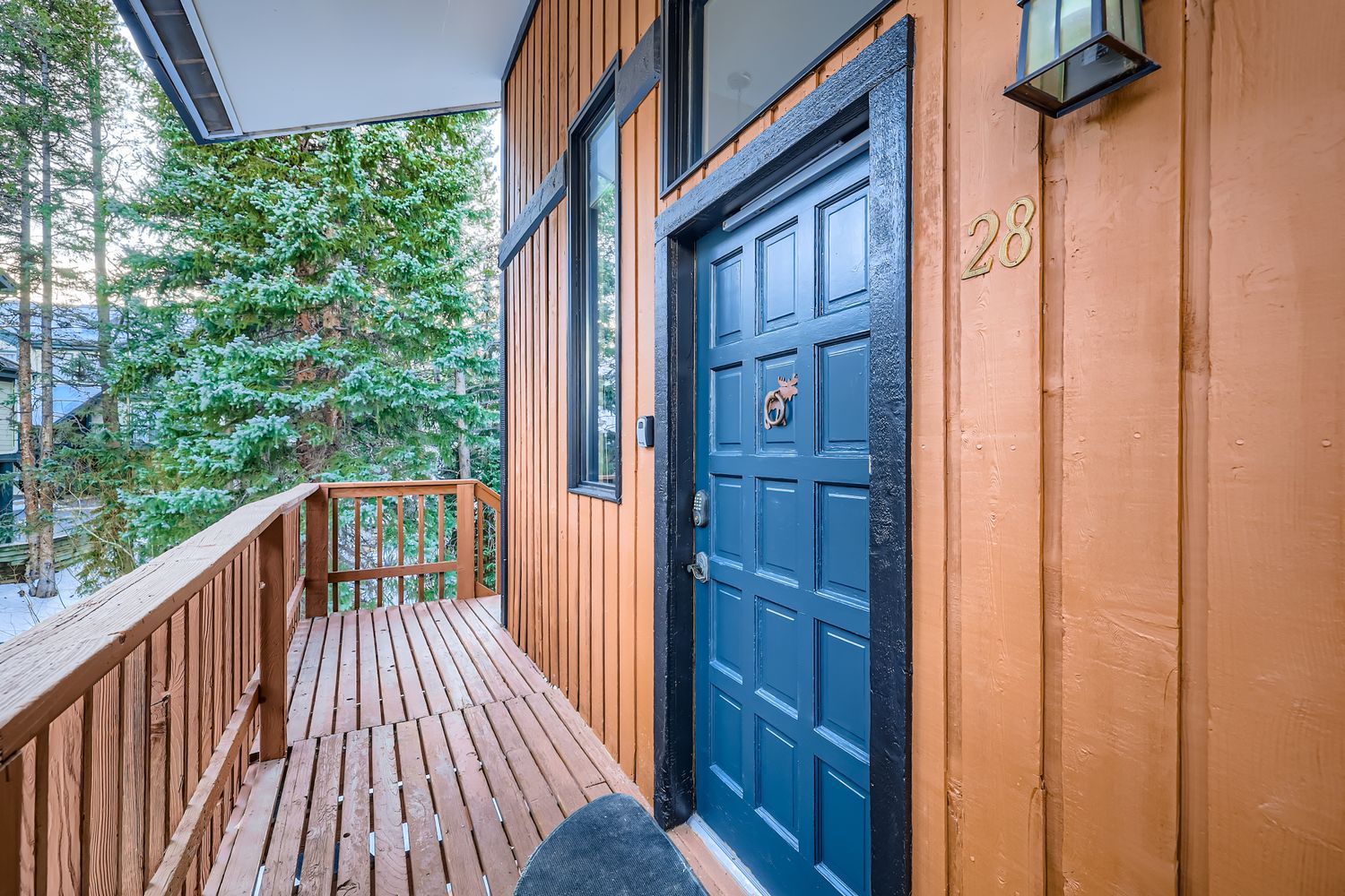 Property entrance featuring orange wood siding, distinctive blue door with decorative knocker, and covered wooden deck surrounded by mature trees.