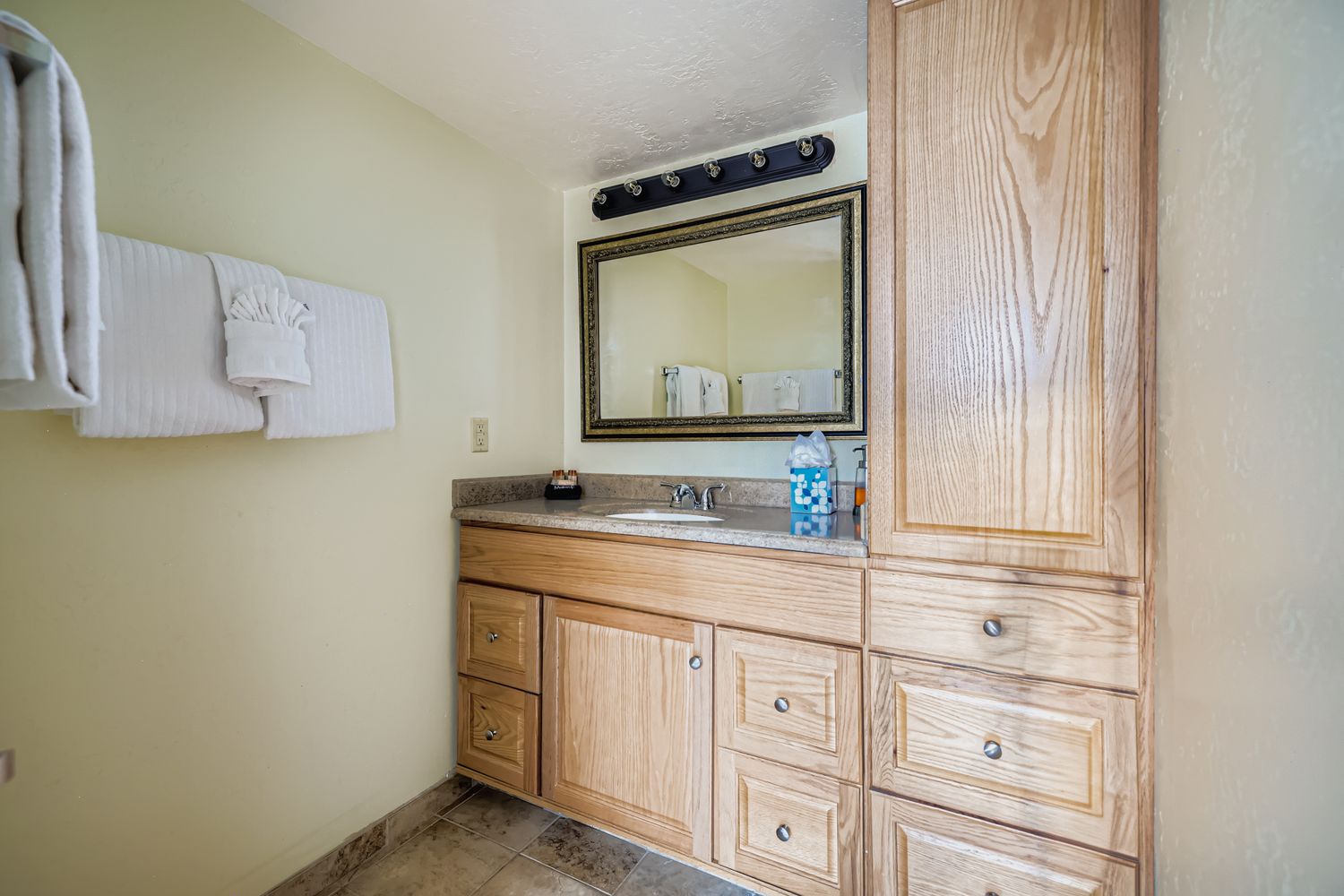 Your private bathroom features a granite vanity with ample storage, fluffy towels, and warm wood cabinetry for a cozy, home-like retreat.